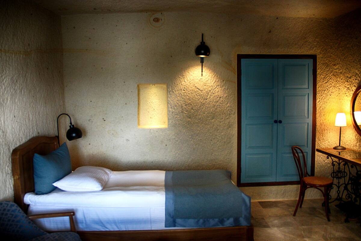 A bedroom with a bed, a chair, a desk with a lamp, and a blue door.