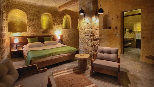 A rustic room with a bed, a wooden chair, and a stone wall.