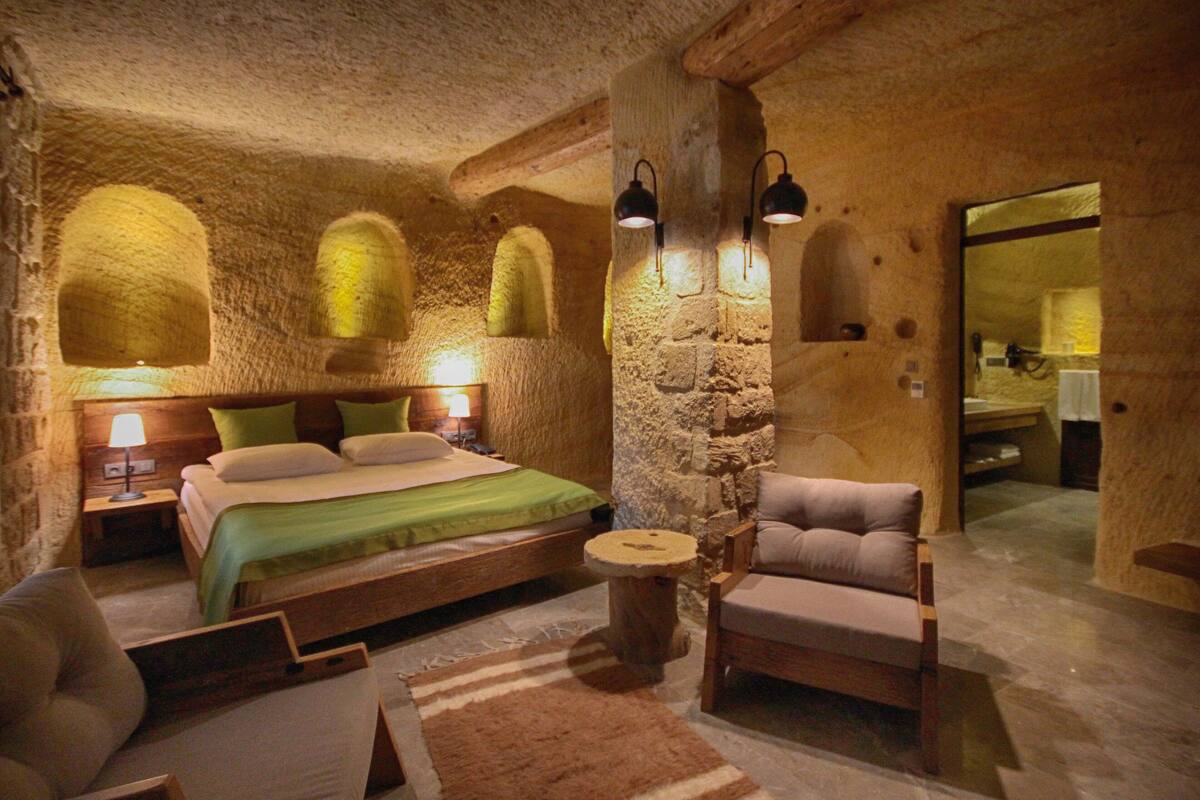 A rustic room with a bed, a wooden chair, and a stone wall.