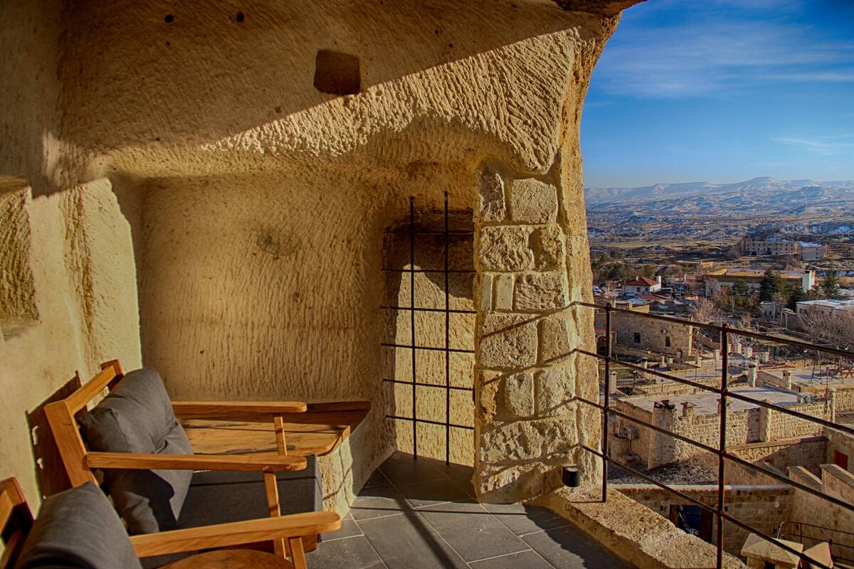 A stone-walled room with a wooden bench and a view of a cityscape.