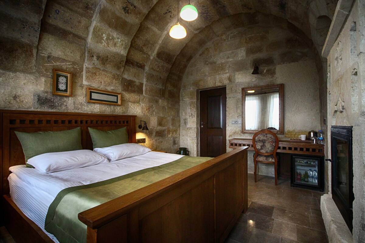 A stone-walled bedroom with a wooden bed, a small kitchenette, and a fireplace.