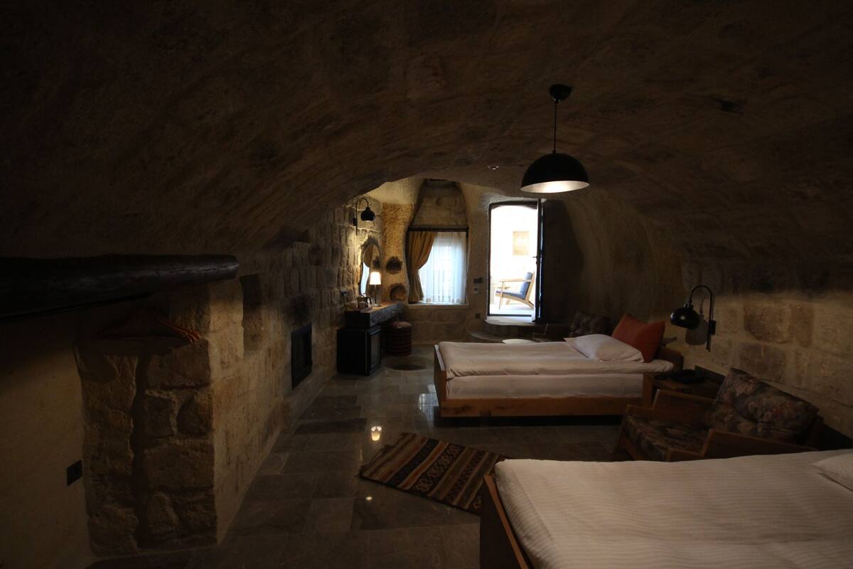 A rustic bedroom with a stone ceiling, a fireplace, a bed with a wooden frame, and a nightstand.