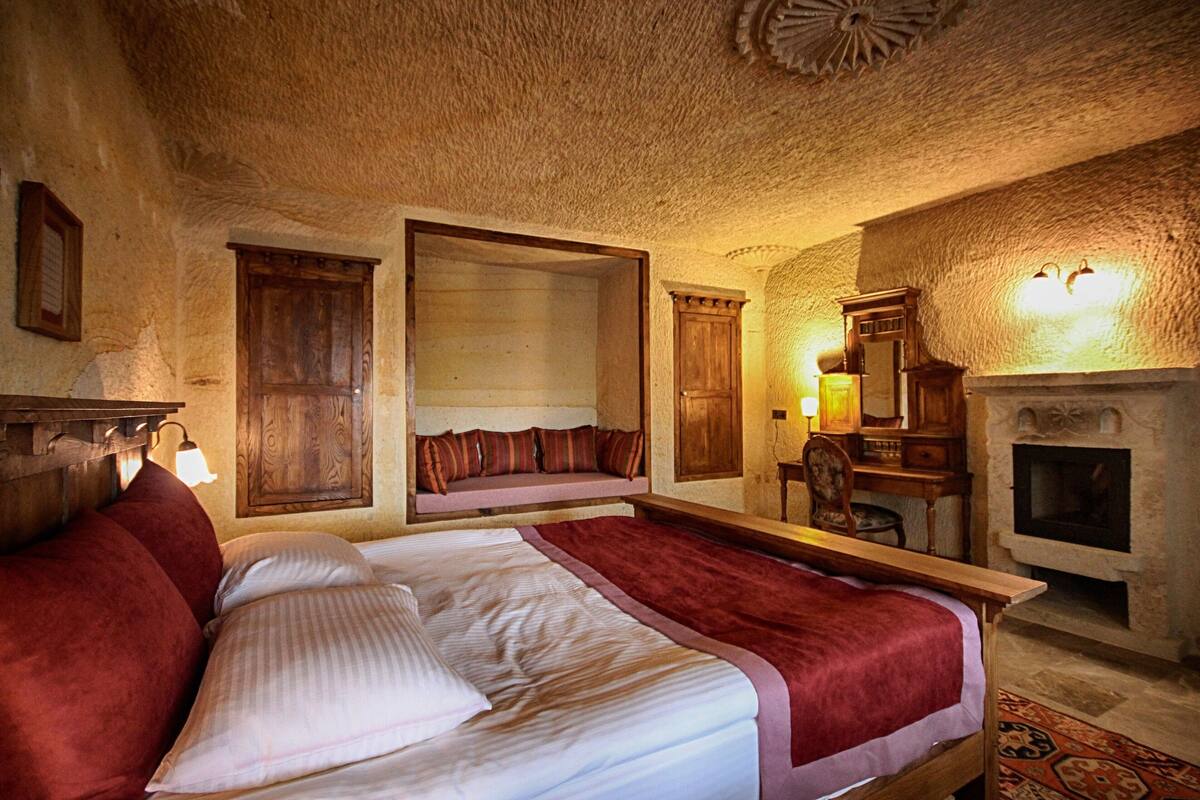 A bedroom with a large bed, a wooden bench, a fireplace, and a desk with a chair.