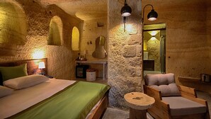 A rustic stone room with a bed, a wooden chair, and a small table.