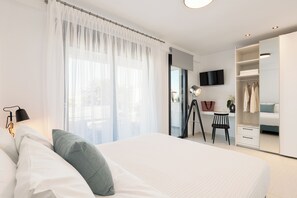 Ein modernes Schlafzimmer mit einem großen Bett, einem Schreibtisch, einem Stuhl, einem Kleiderschrank und einem Fernseher.