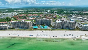 An aerial view of a coastal resort with multiple high-rise buildings, a sandy beach, and a clear blue sky.
