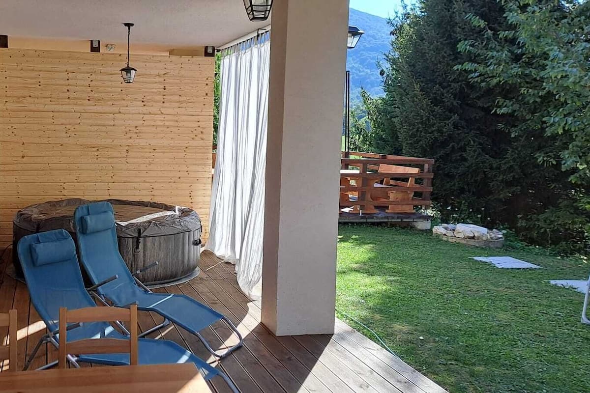 A covered outdoor seating area with a wooden deck, a blue lounge chair, and a wooden table.