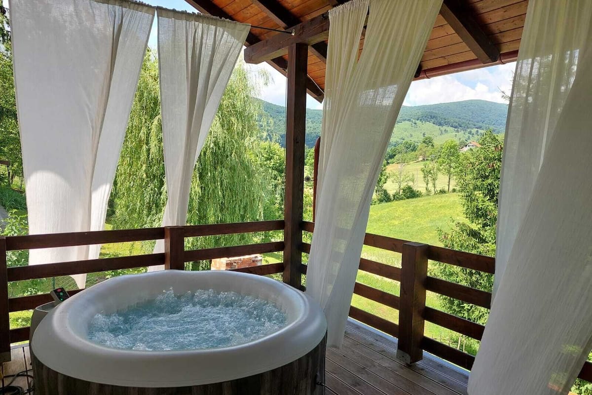 A hot tub on a wooden deck with a view of a green landscape.