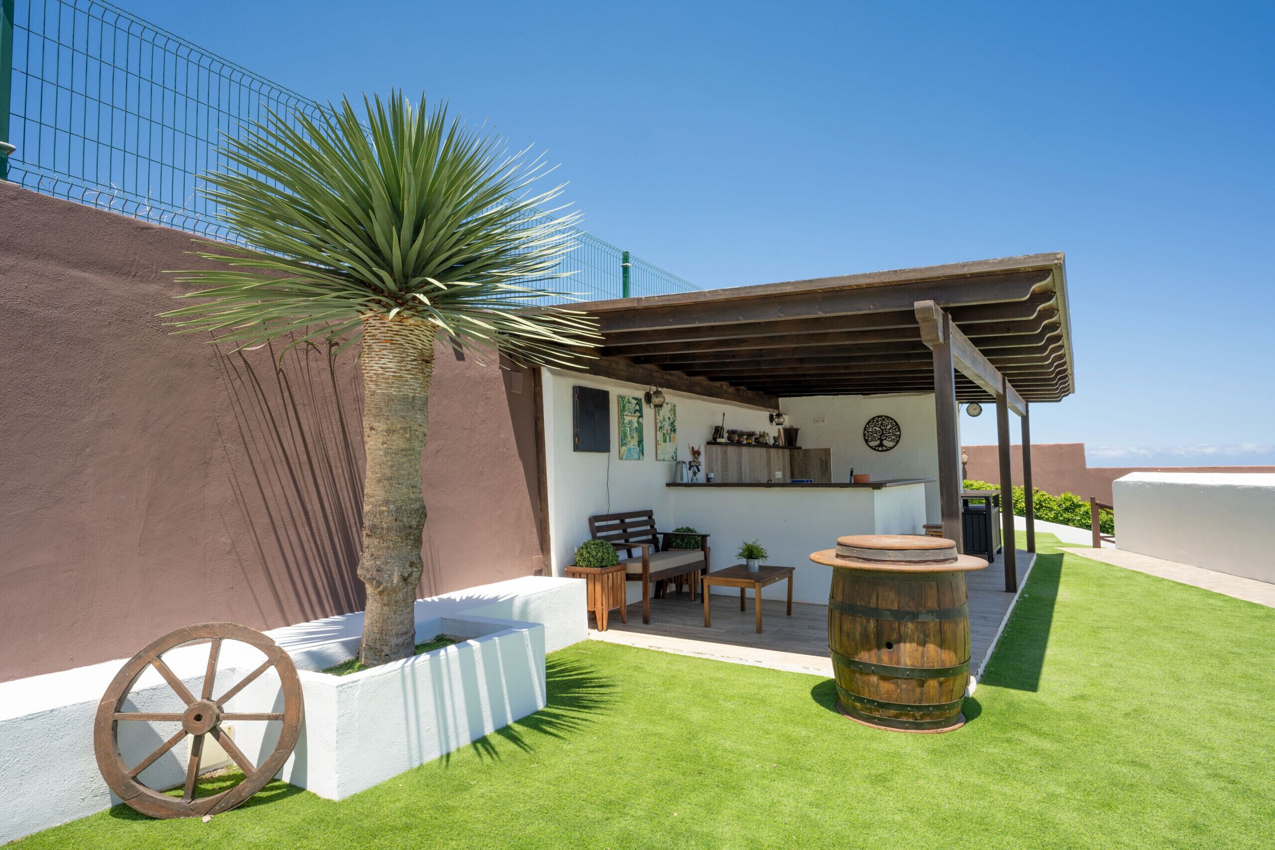 Un'area patio con una botte di legno, una palma e una fioriera bianca.