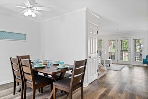 A dining area with a wooden table and chairs, a ceiling fan, and a view of the outdoors through a door.