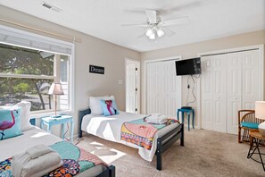 A bedroom with a bed, a TV, a ceiling fan, and a window with blinds.