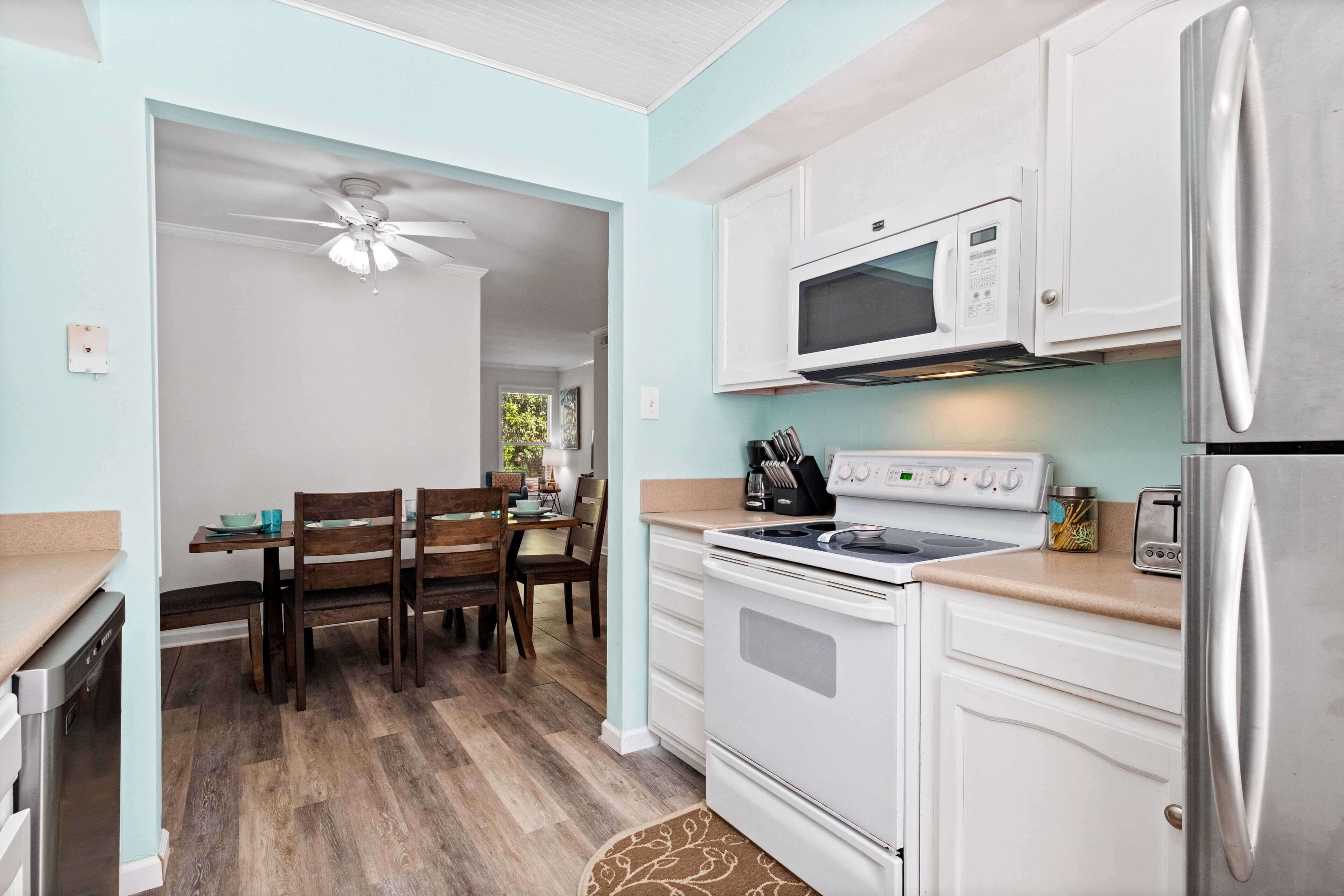 A compact kitchen with white cabinets, a microwave, a stove, and a refrigerator.