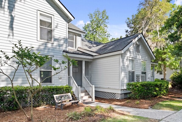 A two-story house with a front porch, a bench, and a sign that says "SEE YOU THERE."