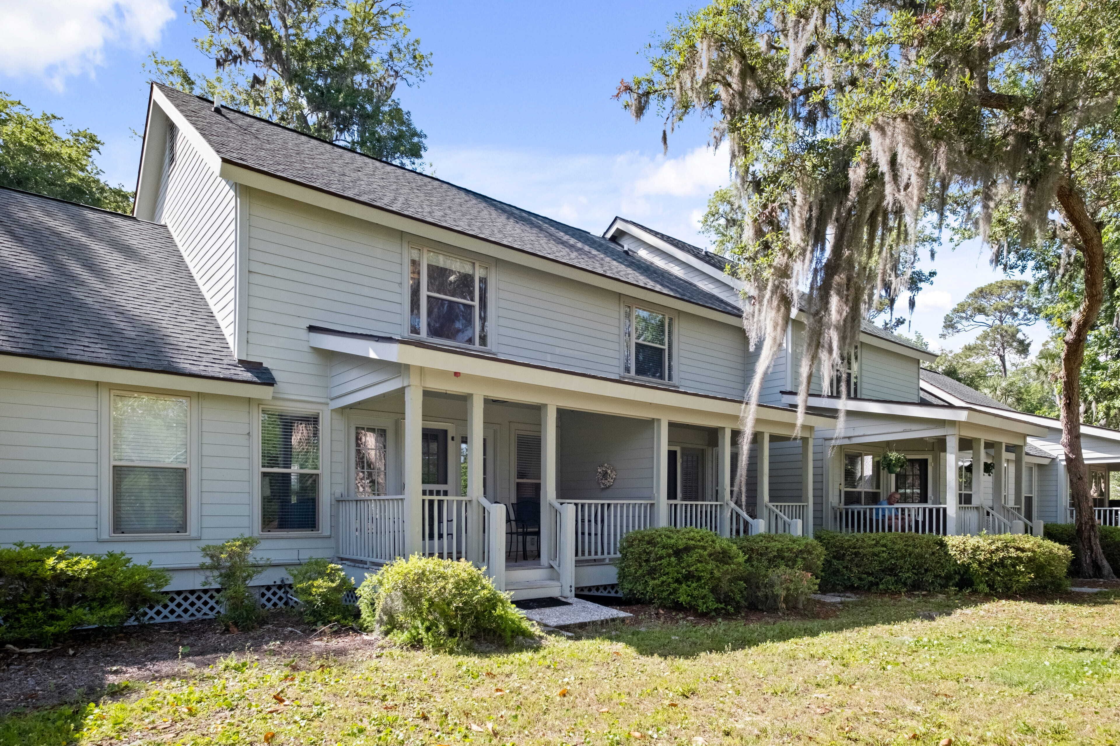 A two-story house with a porch, a covered front porch area, and a small front yard with bushes and a tree.