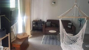 Uma sala de estar com um sofá marrom, uma cadeira suspensa branca, uma mesa redonda pequena e um tapete estampado.
