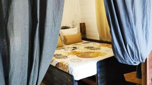 Quarto com cama, cortinas, um banco de madeira e luminária pendente.