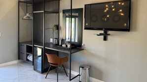 A modern bedroom with a built-in desk, a TV mounted on the wall, a chair, and a small trash can.