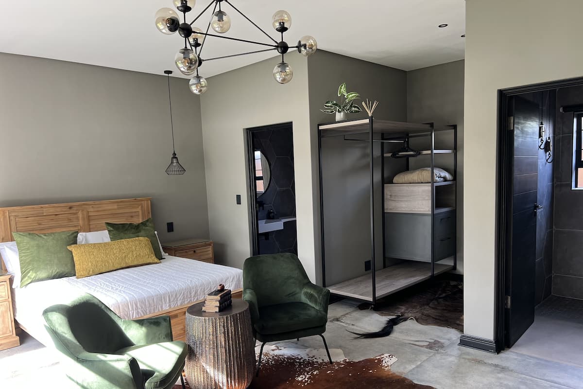 Een moderne slaapkamer met een bed, groene stoelen, een bijzondere lamp en een kapstok.