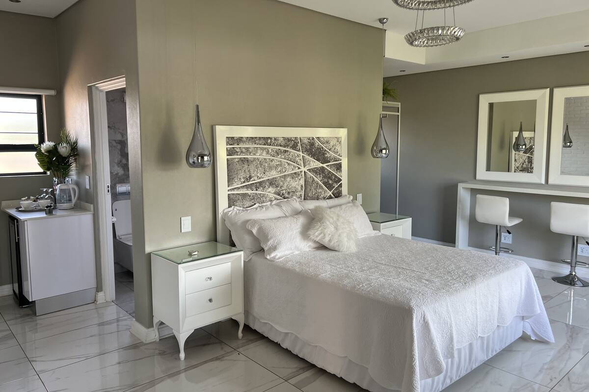 Een moderne slaapkamer met een groot bed, nachtkastjes, een kaptafel en een spiegel.