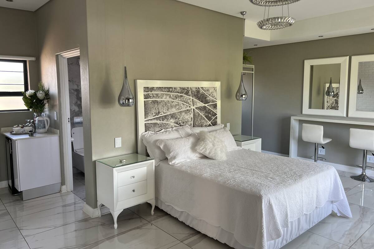 Een slaapkamer met een bed, nachtkastjes, een kast, een kaptafel met spiegel en een kroonluchter.