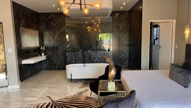 A modern bedroom with a large bed, a glass bedside table, a zebra-patterned rug, and a black and white marble wall.