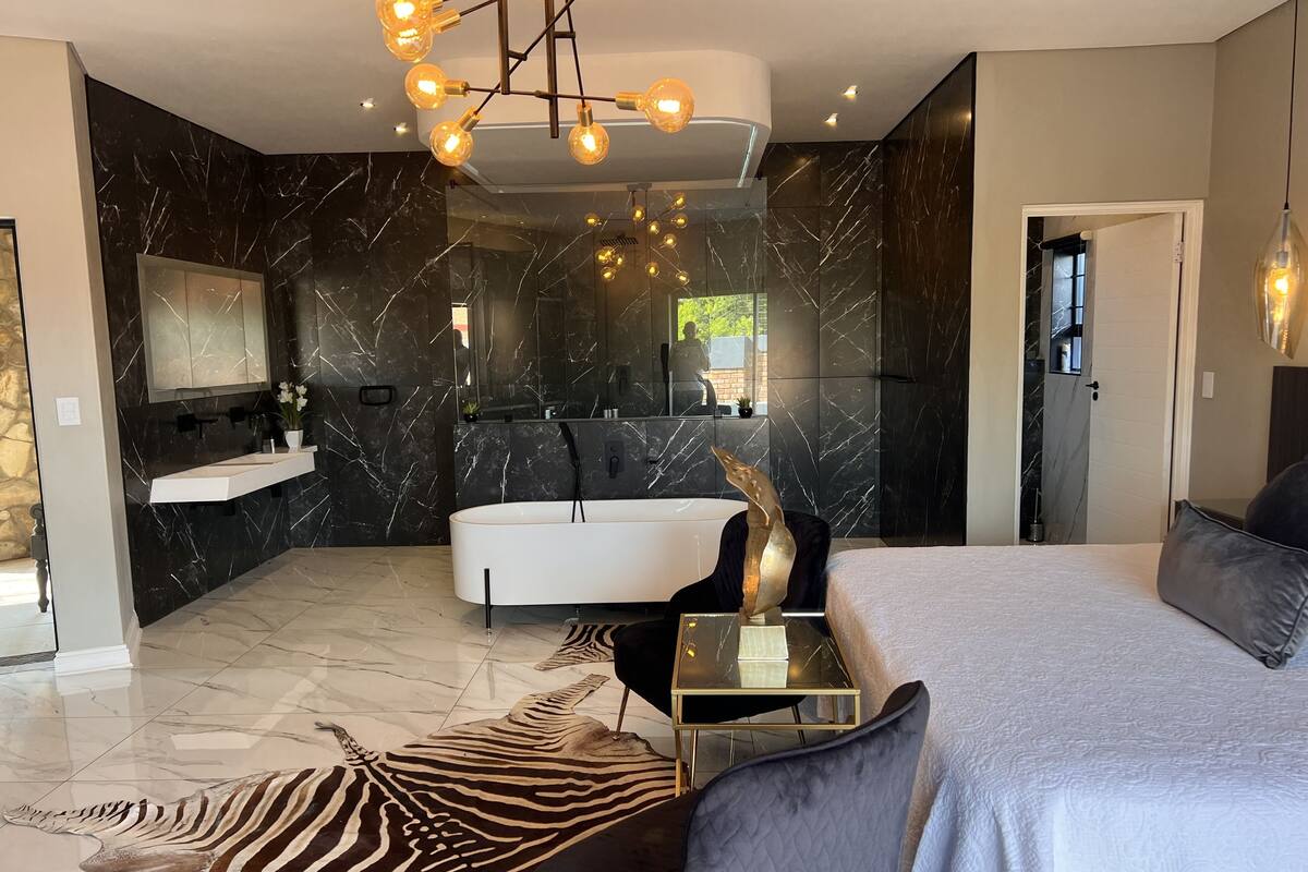Een moderne slaapkamer met een groot bed, een glazen nachtkastje, een vloerkleed met zebraprint en een wand van zwart-wit marmer.