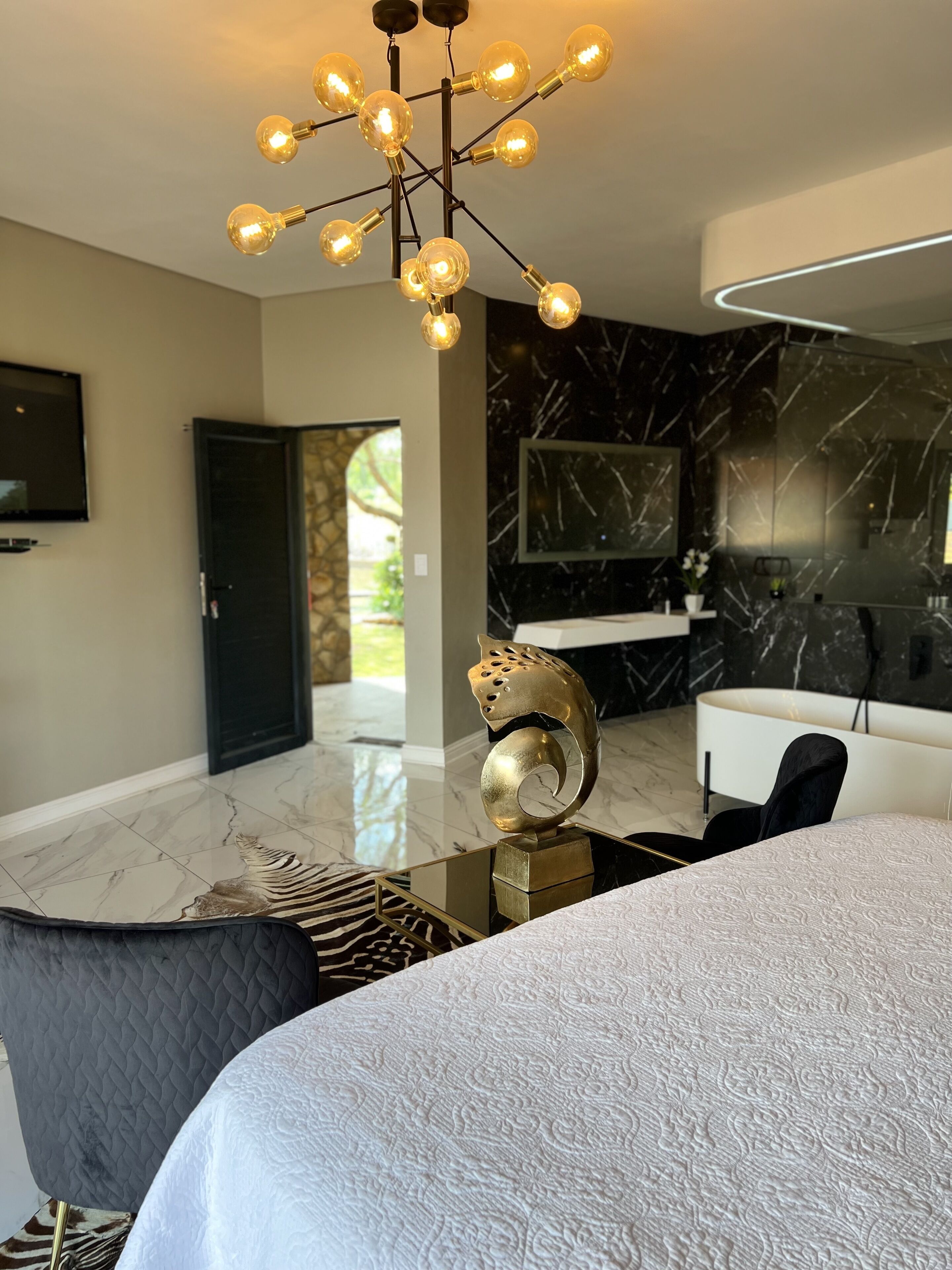 A modern bedroom with a bed, a unique gold sculpture, a black and white marble wall, a black door, and a TV mounted on the wall.