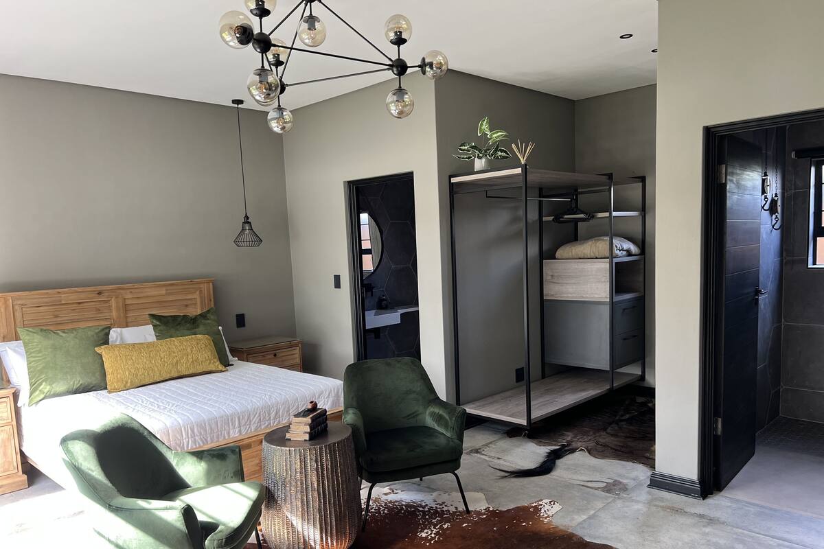 Slaapkamer met een bed, groene stoelen, een rond bijzettafeltje, een hanglamp, een kast en een kleden van koeienhuid.