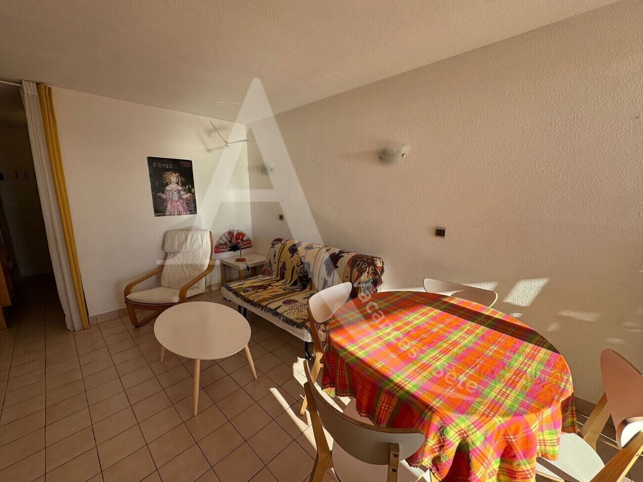 A dining area with a round table covered by a plaid tablecloth, surrounded by chairs.