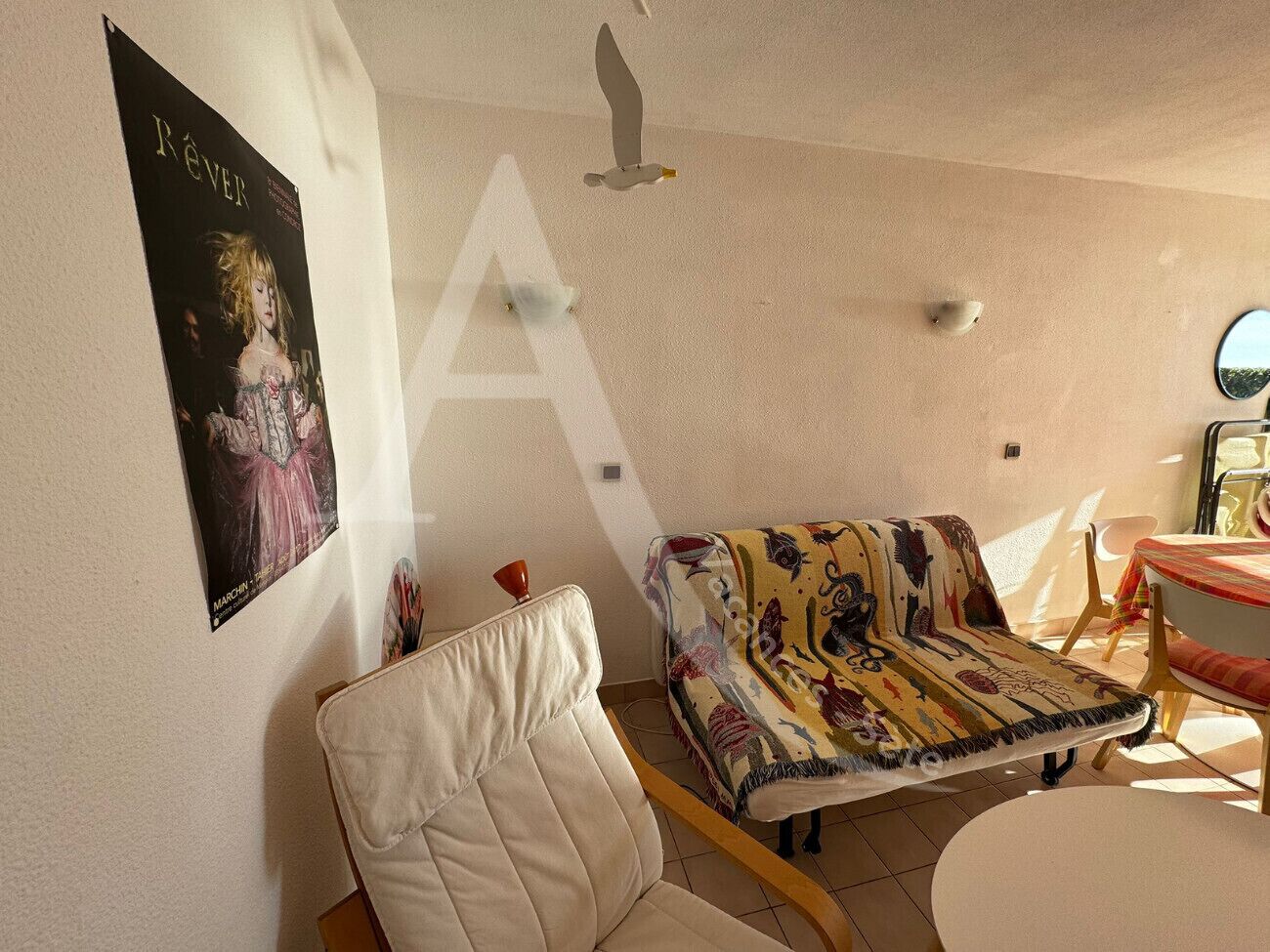 Una sala de estar con un sofá blanco, una manta colorida, una mesita y un cartel en la pared.