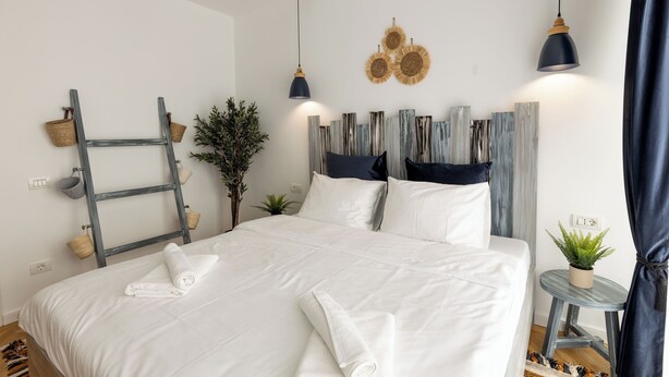 A neatly made bed with white linens and rolled towels, a small side table with a plant, and a ladder against the wall. - Metropole Apartments Panoramic Ateneum (Bucharest)