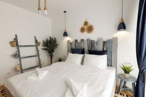 A neatly made bed with white linens and rolled towels, a small side table with a plant, and a ladder against the wall. - Metropole Apartments Panoramic Ateneum (Bucharest)
