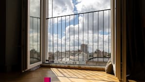 A room with a large window, wooden flooring, and a view of a cityscape. - Metropole Apartments Panoramic Ateneum (Bucharest)