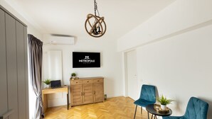 A modern living room with a herringbone floor, a wooden desk, a blue sofa, and a mounted TV. - Metropole Apartments Panoramic Ateneum (Bucharest)