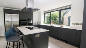 Une cuisine moderne dotée d’un îlot central, de tabourets de bar, d’appareils électroménagers intégrés et d’une fenêtre offrant une vue sur la verdure.