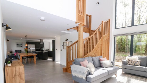 Un vaste espace de vie comprenant une cuisine moderne, un escalier en bois et une grande fenêtre donnant sur l’extérieur.