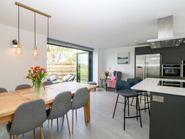 A modern kitchen with a wooden dining table, grey chairs, and a built-in oven.