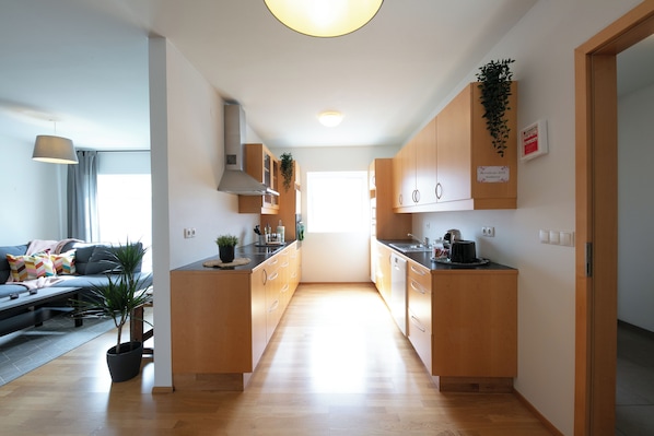 A modern kitchen with wooden cabinets, a central island, and a dining area with a sofa and table. - The Private Apartments (Borgarnes)