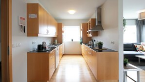 A modern kitchen with wooden cabinets, a central island, and a view to the living area. - The Private Apartments (Borgarnes)