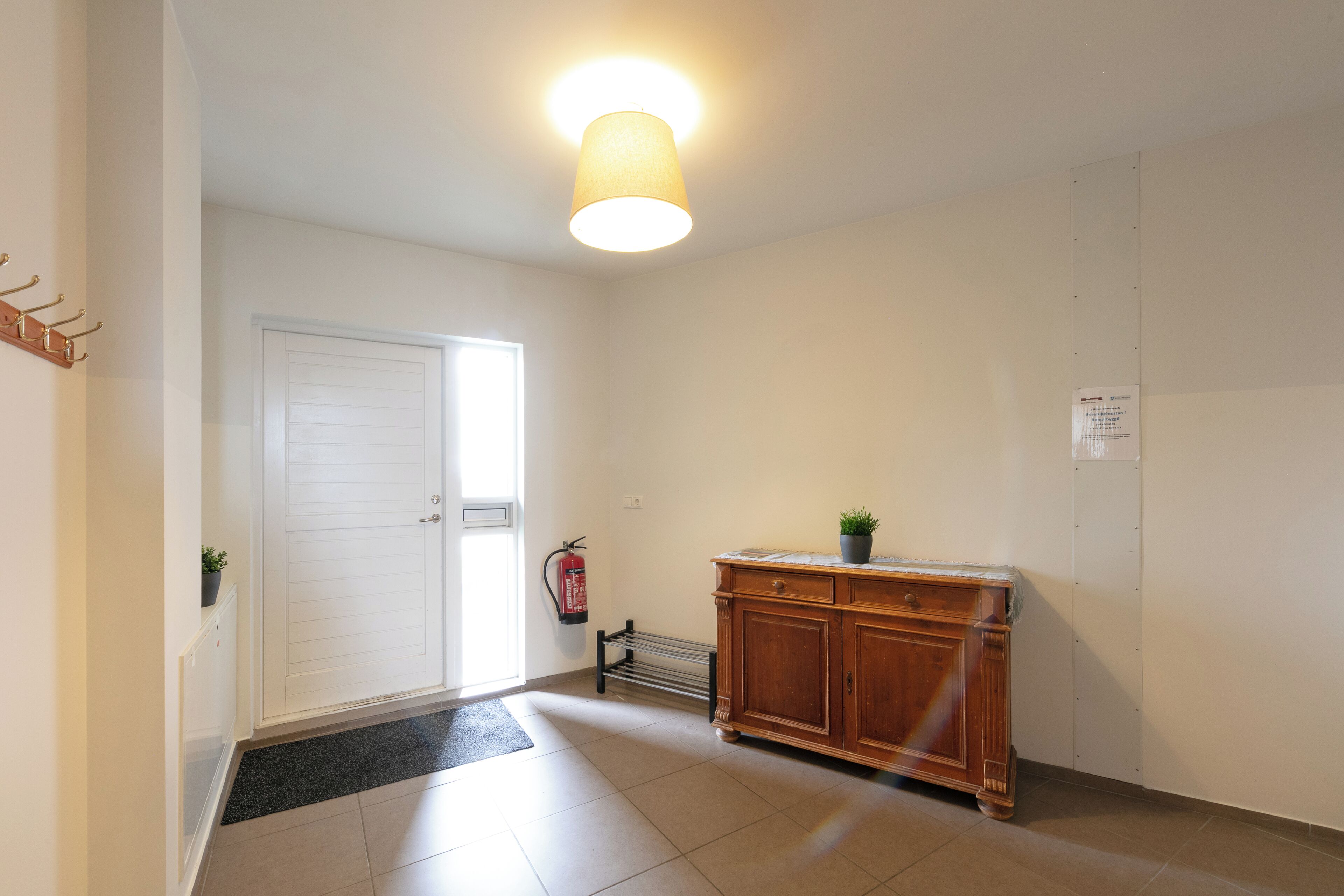 A hallway with a white door, a radiator, a wooden cabinet, and a fire extinguisher.