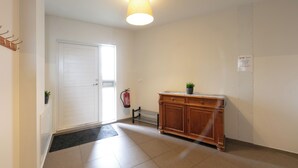 A hallway with a white door, a radiator, a wooden cabinet, and a fire extinguisher. - The Private Apartments (Borgarnes)