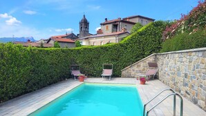 Piscina rectangular con una escalera metálica, rodeada de muros de piedra y un seto.