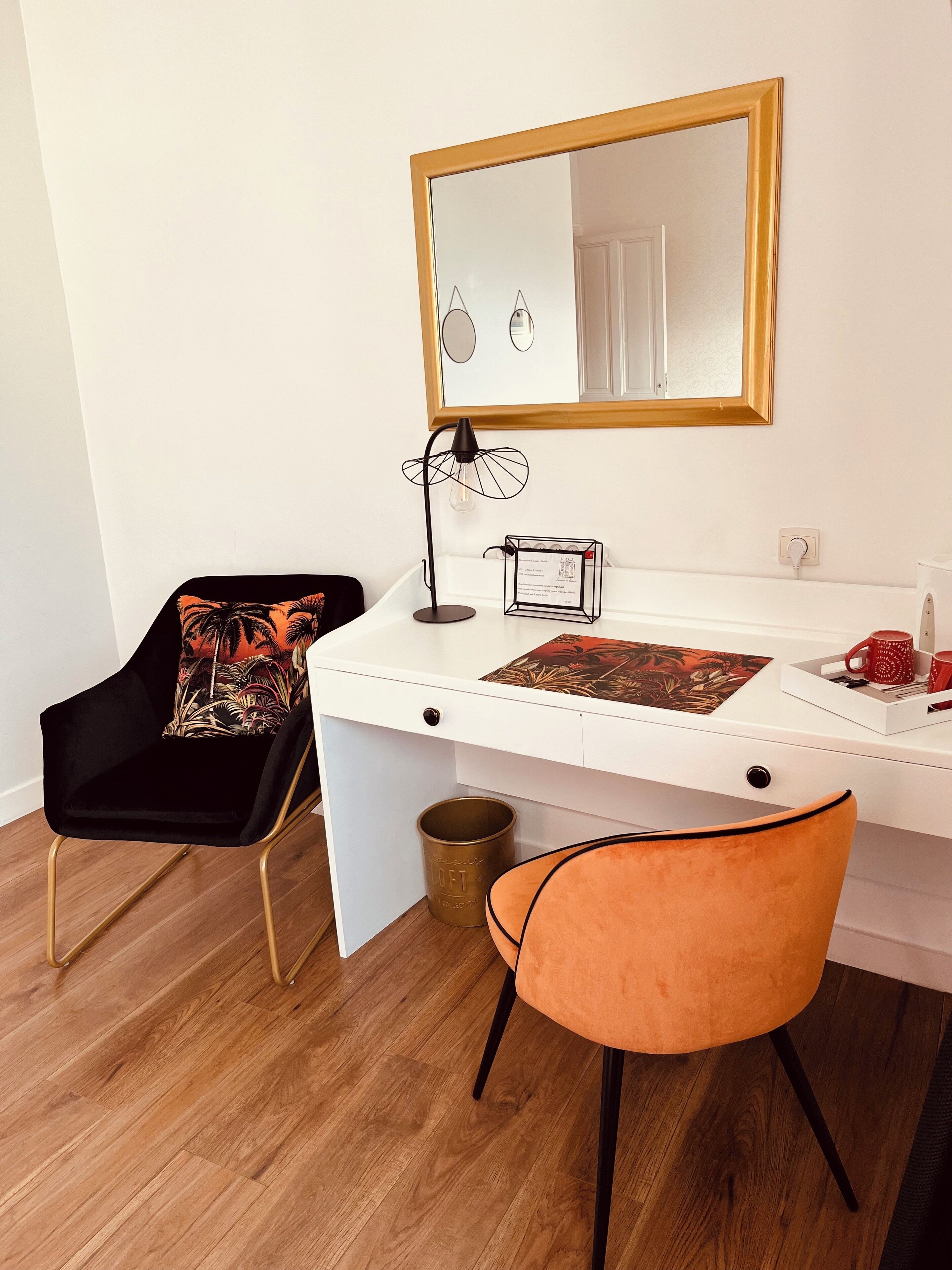 Un bureau blanc avec un miroir, une lampe et un plateau contenant des tasses et un livre.