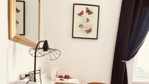 A modern room with a white desk, a black chair, and a large mirror. There is a framed botanical print on the wall and a black curtain partially drawn. - La maison de Louisette (Le Faouet)