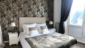 A bedroom with a large bed, two bedside tables, a radiator, and a window with curtains. - La maison de Louisette (Le Faouet)
