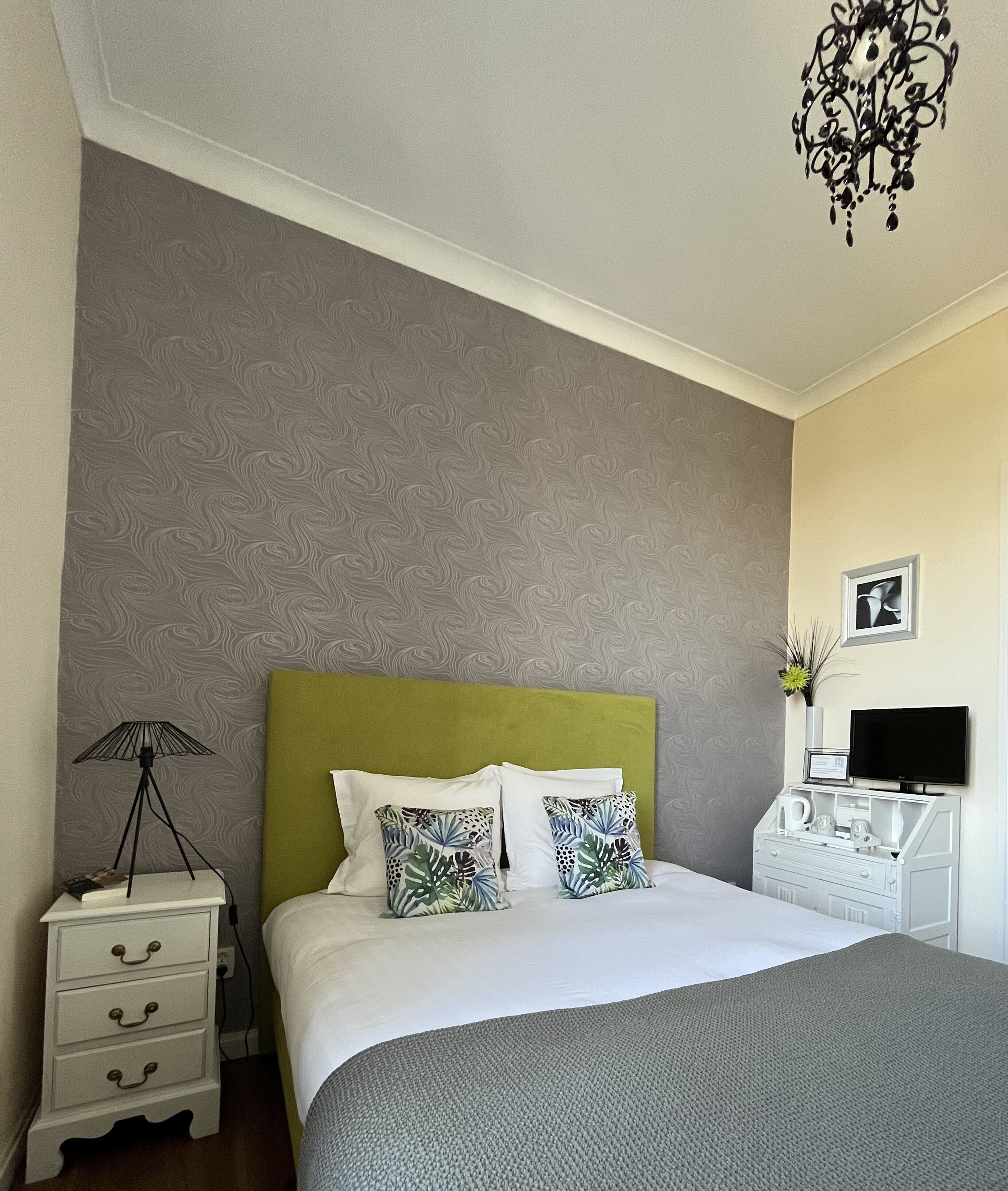 Une chambre à coucher bien rangée, avec un lit, des tables de chevet, une lampe, un téléviseur et un tableau accroché au mur.