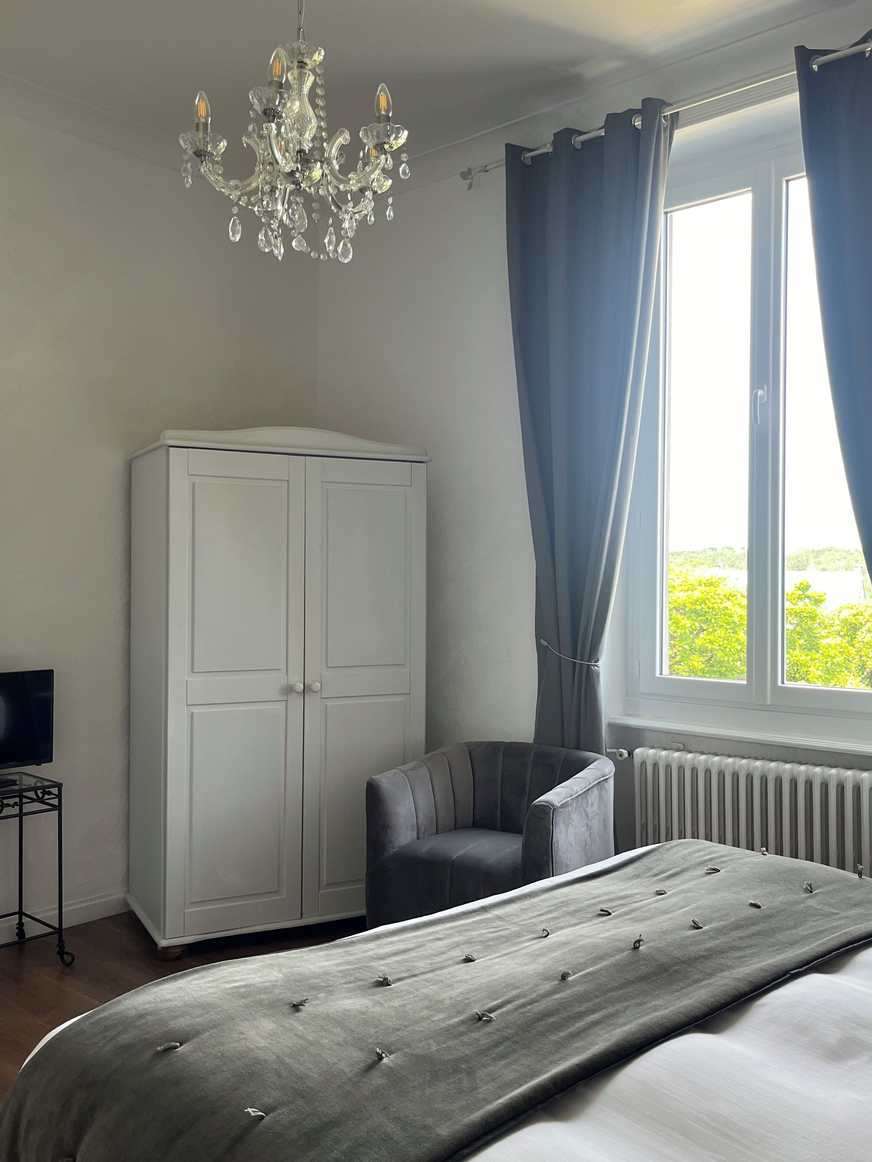 A bedroom with a bed, a wardrobe, a chair, a TV, and a window with curtains.