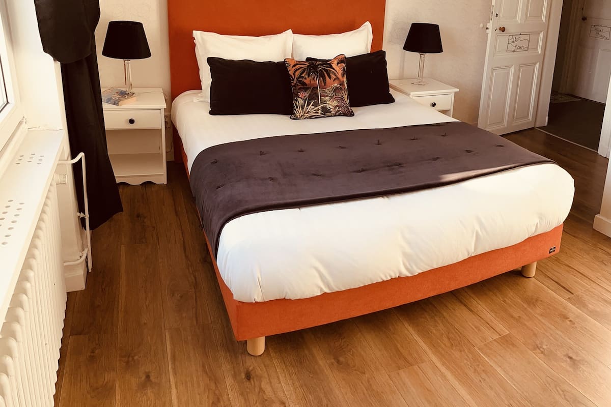 Une chambre à coucher avec un grand lit, deux tables de chevet avec des lampes, une porte et un radiateur.