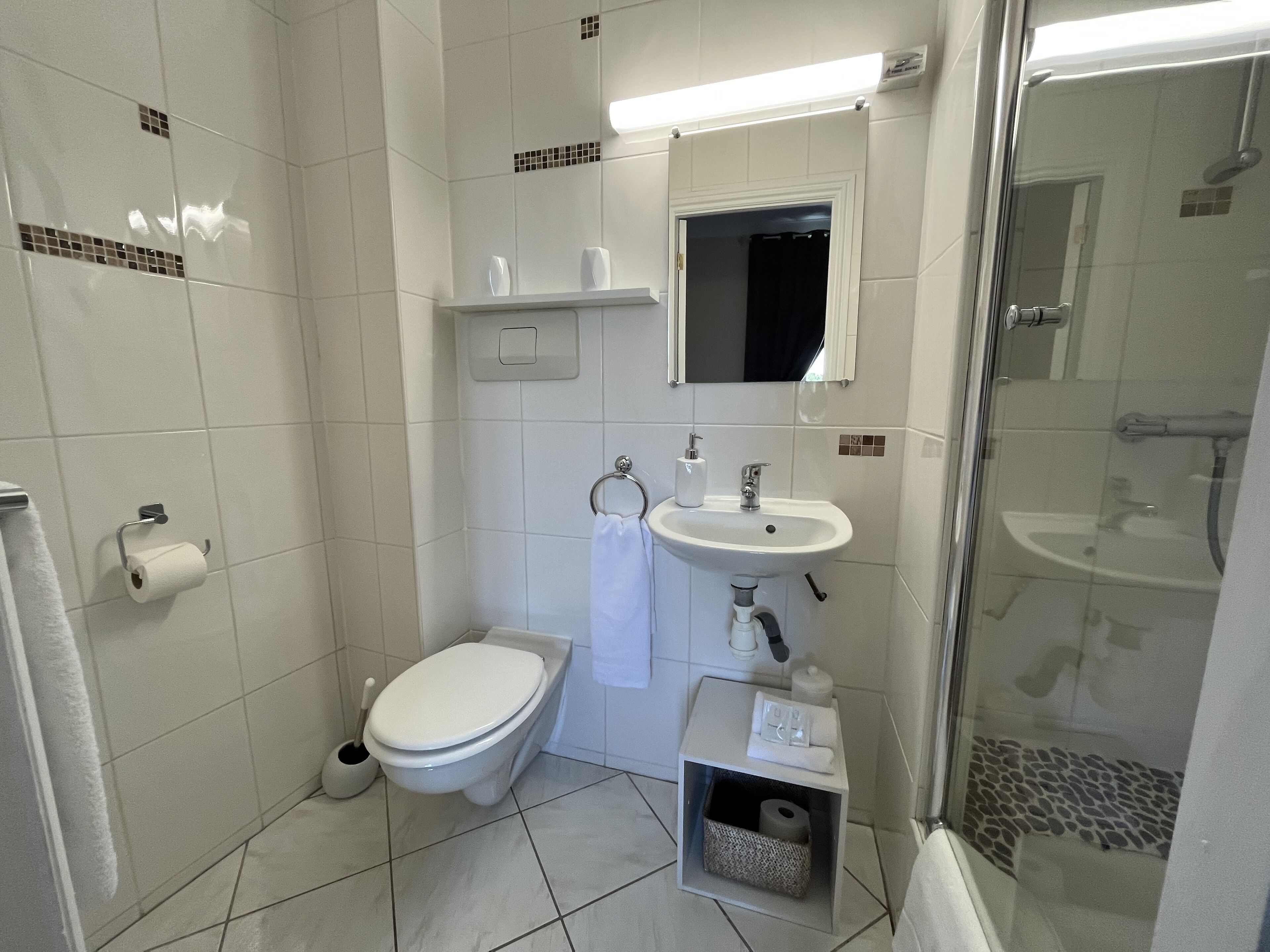 Casa de banho pequena e moderna com sanita, lavatório e chuveiro.