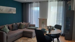 Ein Wohnzimmer mit einer Couch, einem Esstisch mit Stühlen, einer Vase mit Blumen und einer Heizung.